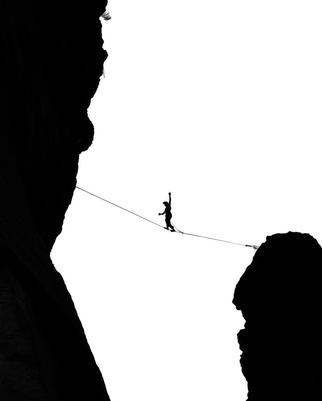 Black and white silhouette highlining between cliff faces