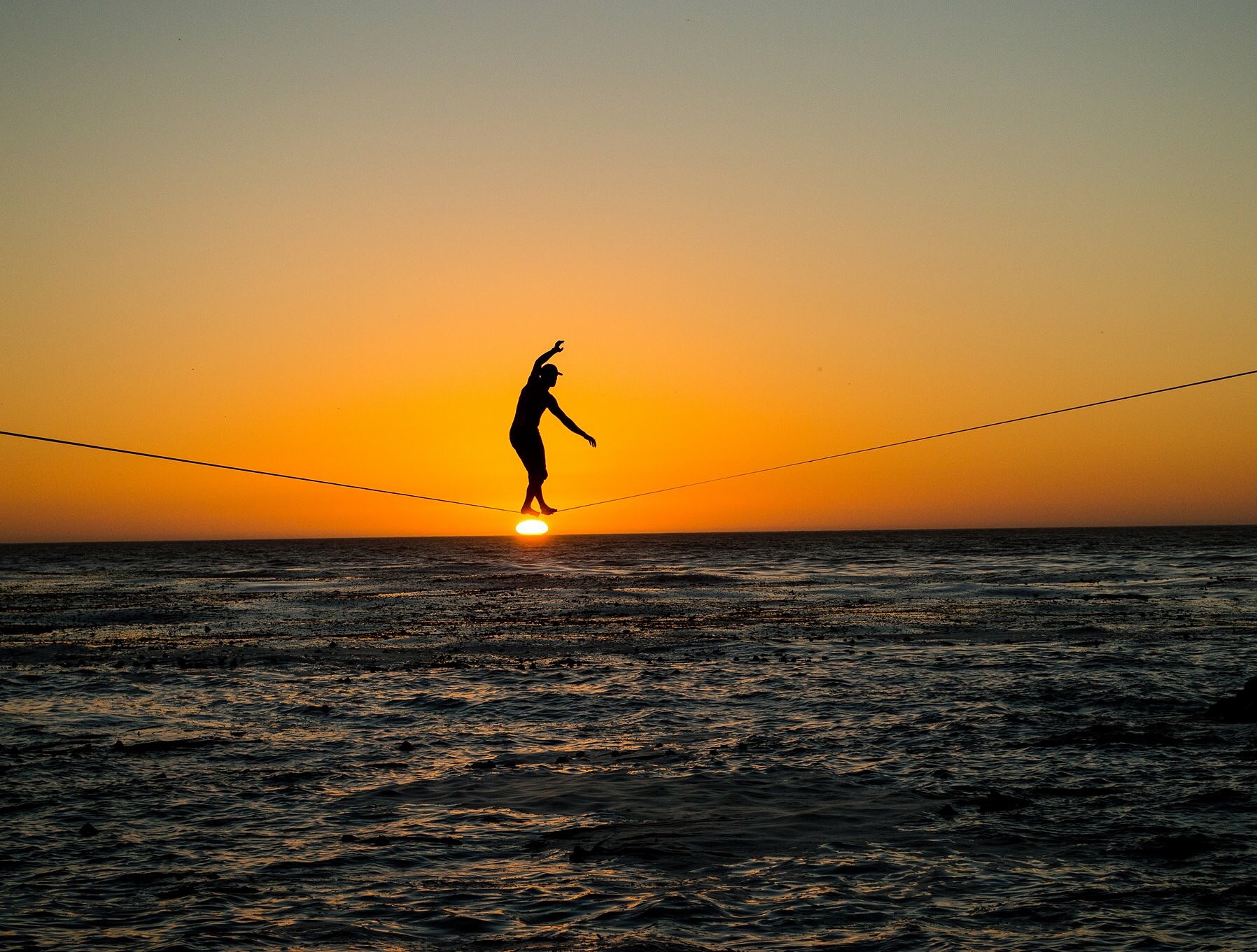 Highlining silhouette at sunset over the ocean